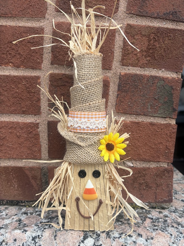 Shim Scarecrow craft on display against a brick wall